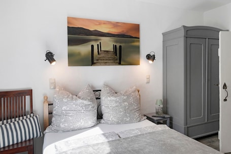 A bedroom with a bed, a headboard, a wardrobe, a nightstand, a lamp, and a painting of a dock.. Holiday Home 'Antje' with Shared Garden and Wi-Fi