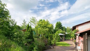 Un sentier de jardin mène à un bâtiment doté d’un toit rouge, qui est entouré d’une végétation luxuriante et d’arbres.