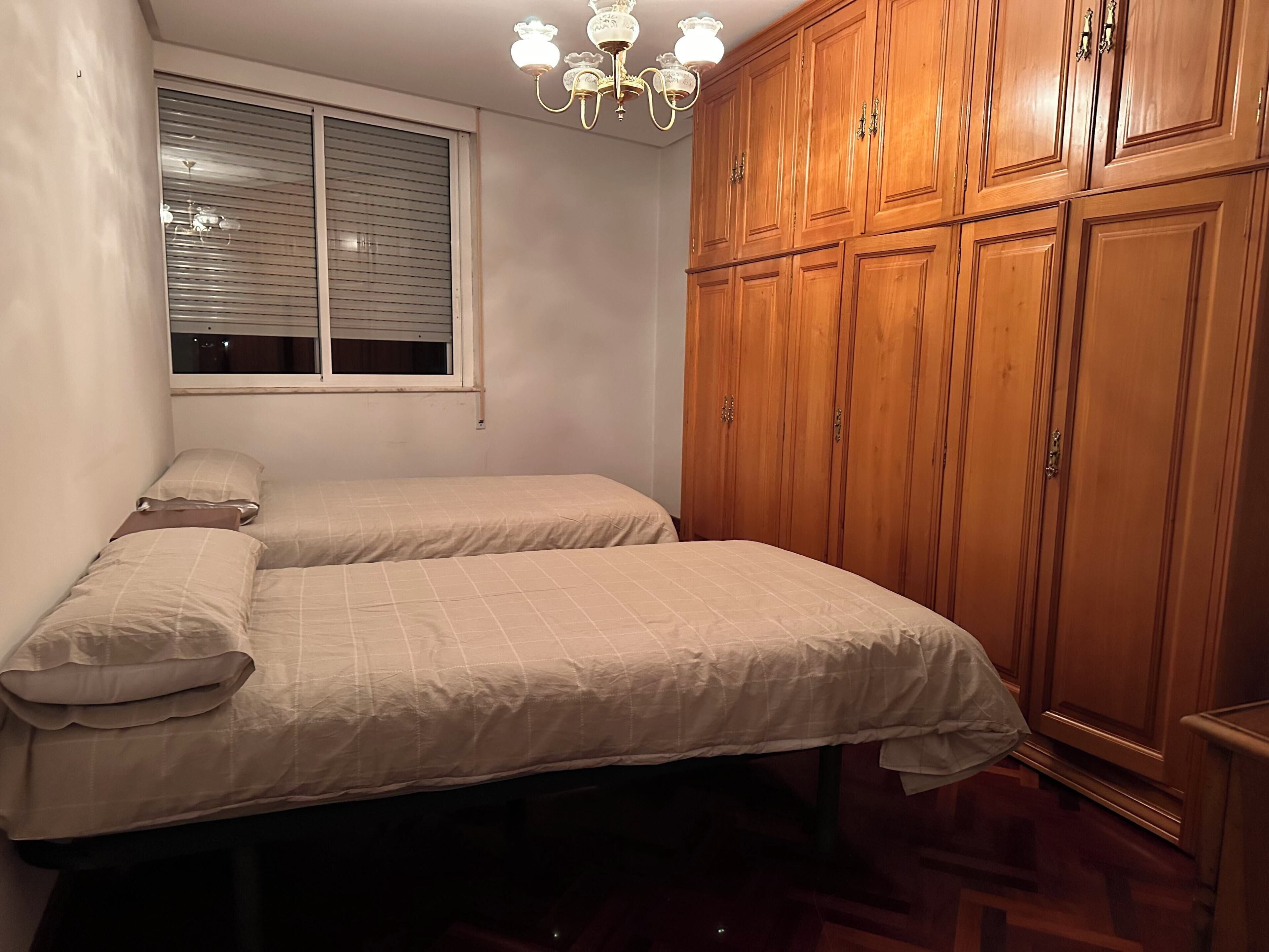 Quarto com duas camas, janela com persianas, um candelabro e armários de madeira.