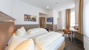 A hotel room with two beds, a desk, a TV, and a painting on the wall. - Hotel Reichshof (Schwerte)