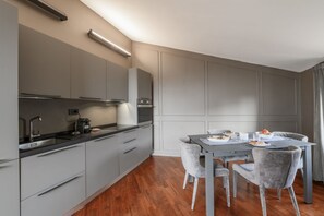 Eine moderne Küche mit grauen Schränken, einer schwarzen Arbeitsplatte und einem Essbereich mit Tisch und Stühlen.