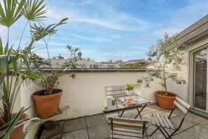 Eine Dachterrasse mit Topfpflanzen, einem Tisch mit Essen und Blick auf Gebäude in der Ferne.
