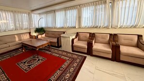 A spacious living room with a red patterned rug, beige sofas, a wooden coffee table, and sheer curtains.