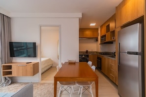 A modern apartment with a wooden dining table, a kitchen with a refrigerator, and a TV in the living area. - Apto com Smart Lock Perto do Aeroporto e Metr (São Paulo)