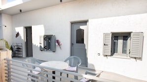 A patio with a table and chairs, a door, and shutters on a white wall.