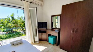 A hotel room with a bed, a desk, a TV, a wardrobe, and a balcony with a view of greenery. - Double room on ground floor (Syvota)