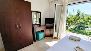 A hotel room with a bed, a desk with a TV, a wardrobe, and a balcony with a view of greenery. - Double room on ground floor (Syvota)
