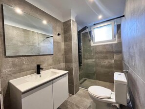 Ein modernes Badezimmer mit einem großen Spiegel, einem weißen Waschbecken, einer Toilette und einer Duschkabine.