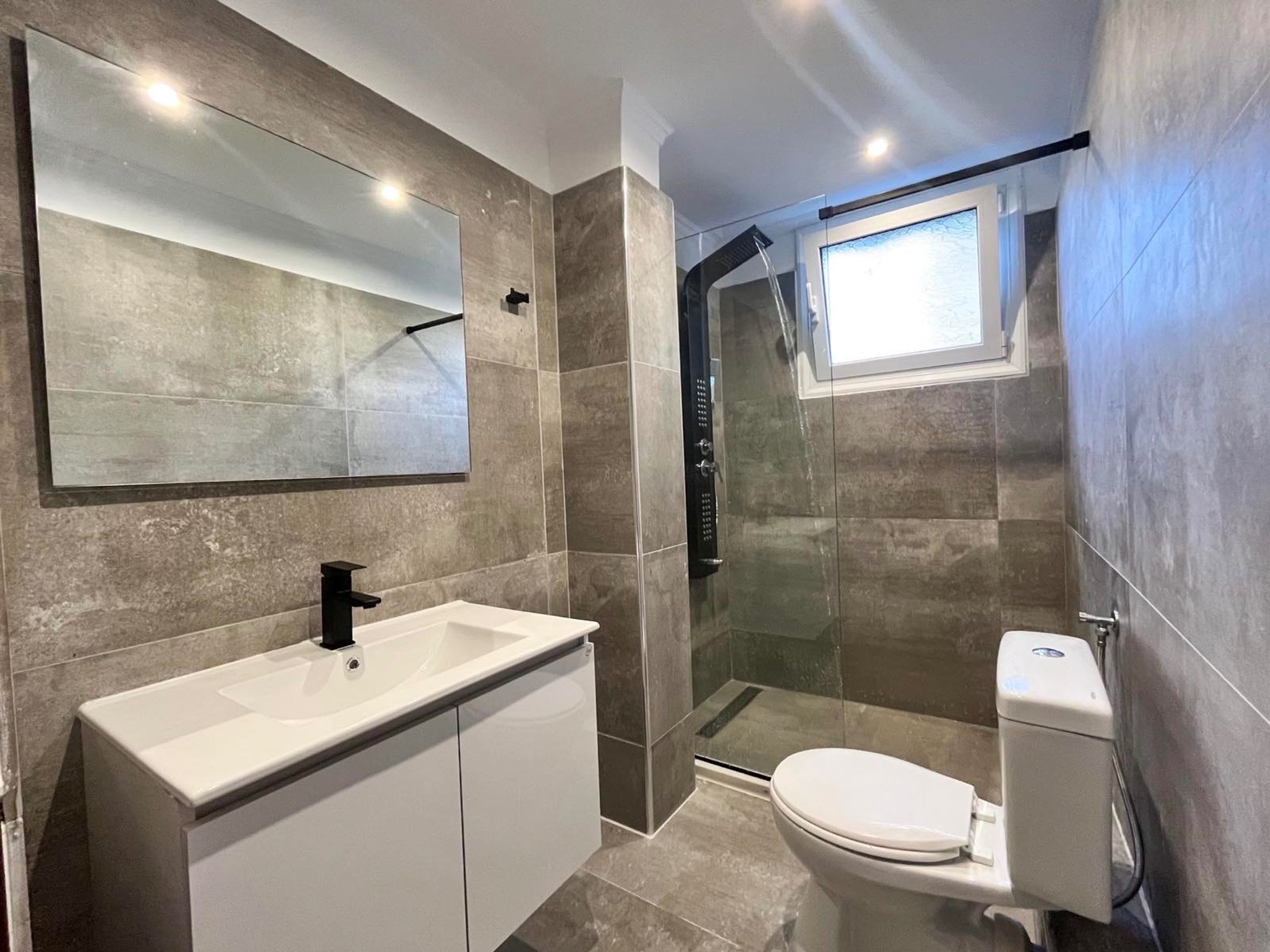 Ein modernes Badezimmer mit einem großen Spiegel, einem weißen Waschbecken, einer Toilette und einer Duschkabine.