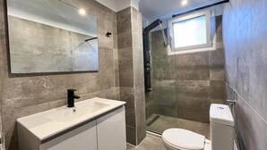 Un baño moderno con un espejo grande, un lavabo blanco, un inodoro y una zona de ducha con mampara de vidrio.