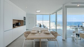Eine moderne Küche mit weißen Schränken, einem Holzespeisetisch mit vier Stühlen und Blick auf den Ozean durch große Fenster.