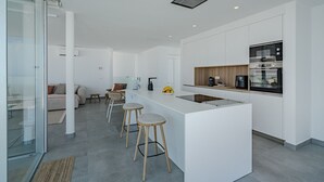 Eine moderne Küche mit Kochinsel, Barhocker, Backofen und Kaffeemaschine.