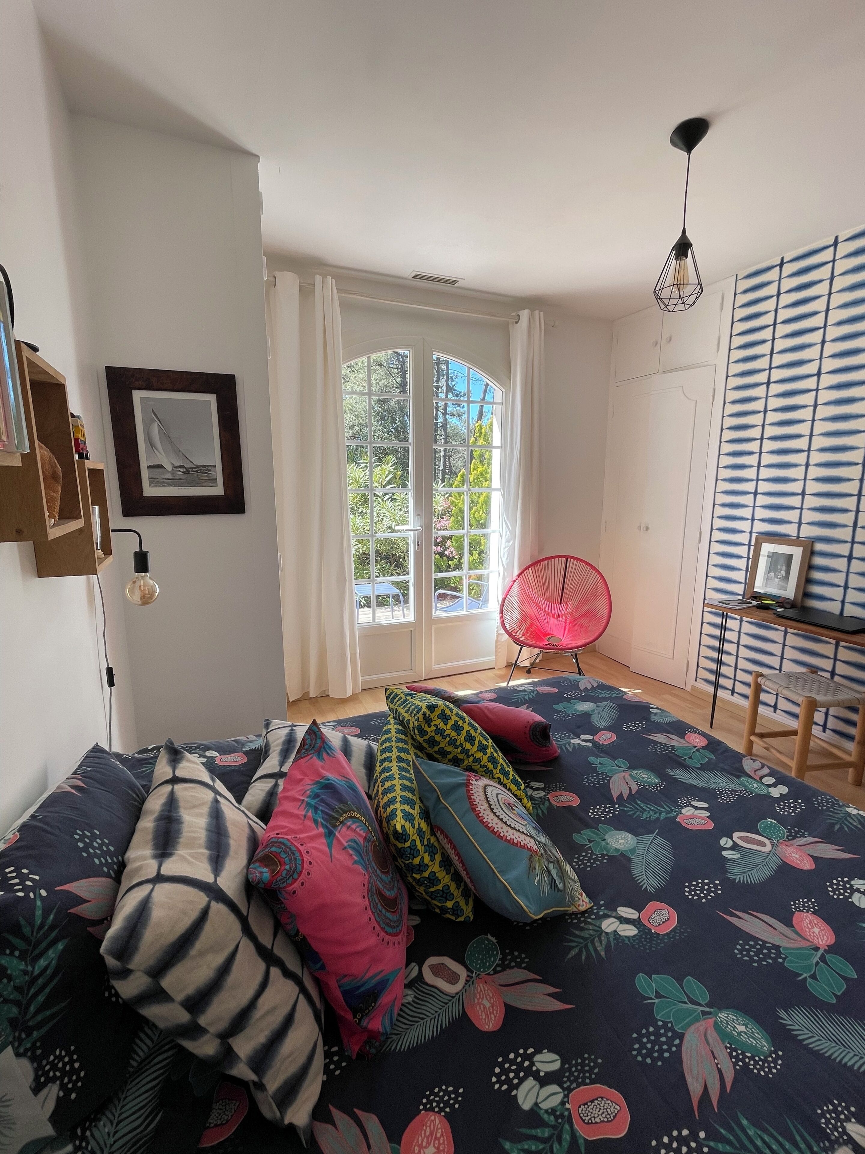 A bedroom with a bed, a red chair, a desk, and a window with curtains.