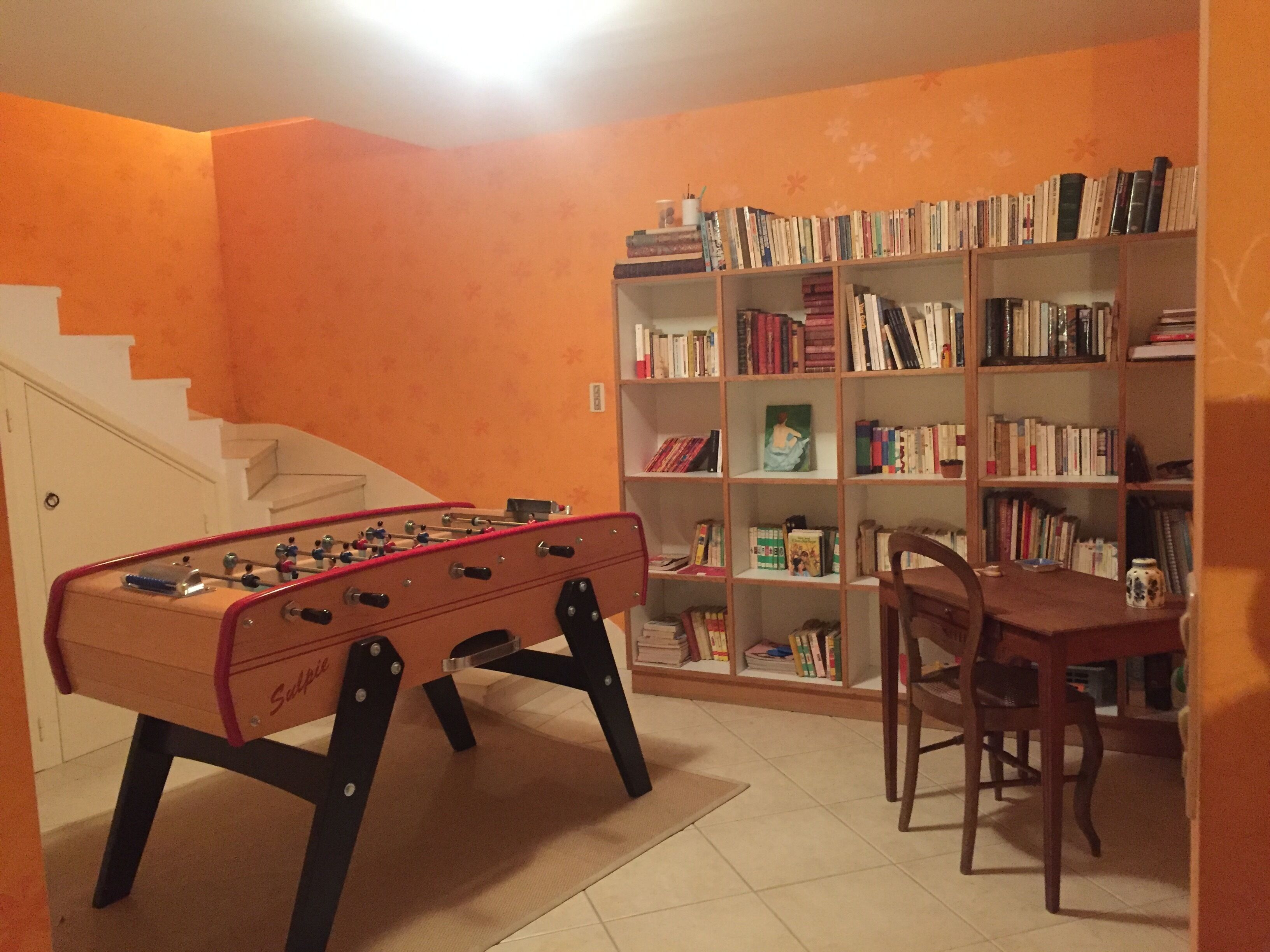 A room with a foosball table, a bookshelf, and a dining area with a chair.