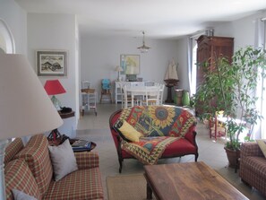A living room with a sofa, a wooden table, a lamp, and a dining area in the background. - Close to the village of L'Herbe Comfortable and spacious villa for 11 people (Lège-Cap-Ferret)