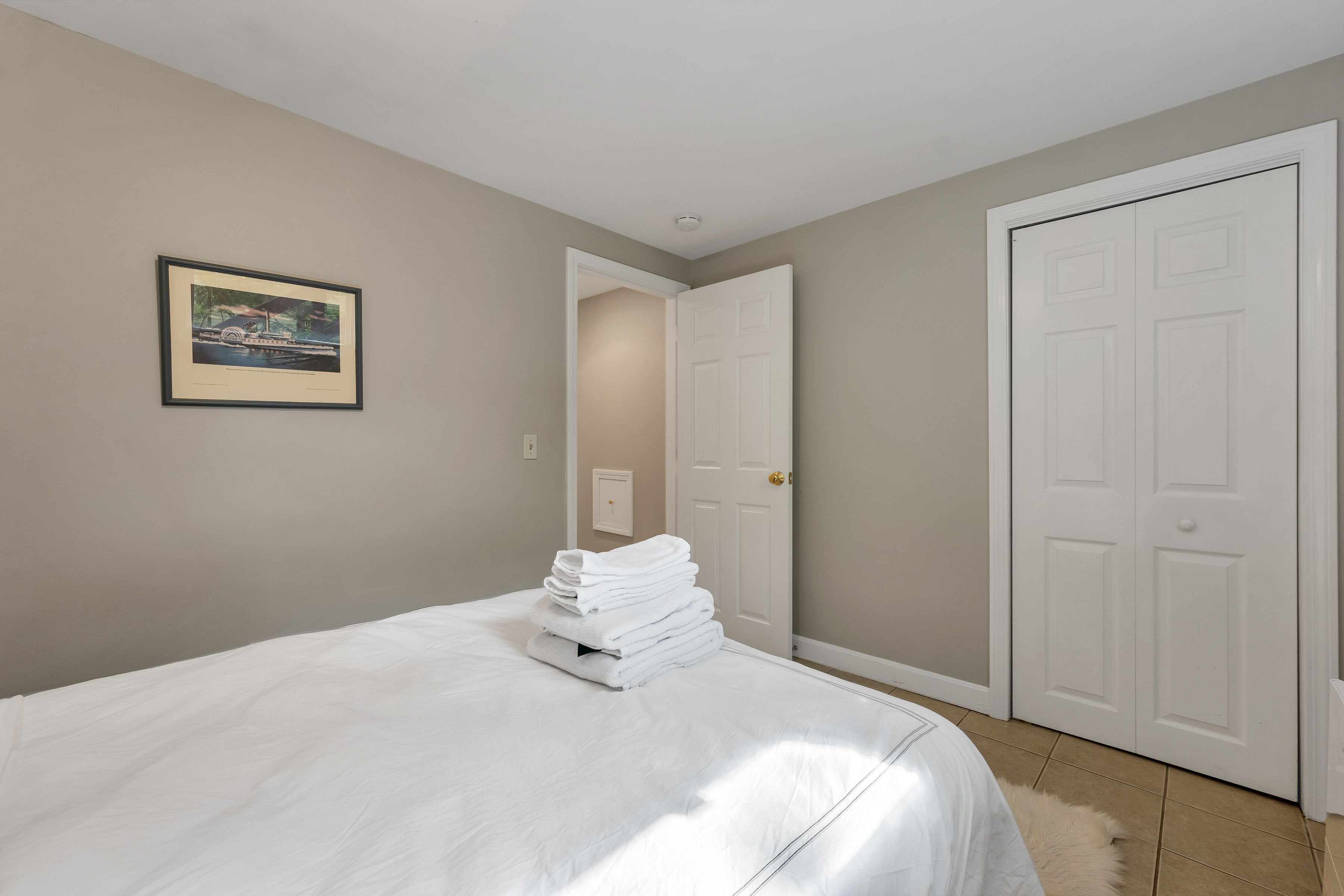 A bedroom with a bed, a framed picture on the wall, and a closed door.