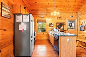 Une cuisine aménagée dans le style d’un chalet, avec des murs en bois, un réfrigérateur, un coin café et une fenêtre offrant une belle vue.