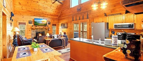 A cabin interior with a wooden interior, a fireplace, a dining area, and a kitchen.