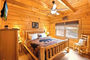 A wooden cabin bedroom with a bed, a ceiling fan, a TV, and a window. - Douglas Lake Cabin Retreat・Beautiful Views・Hot Tub (Sevierville)
