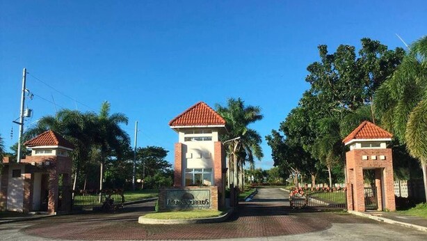 Una entrada con portón, un letrero, un camino y palmeras.