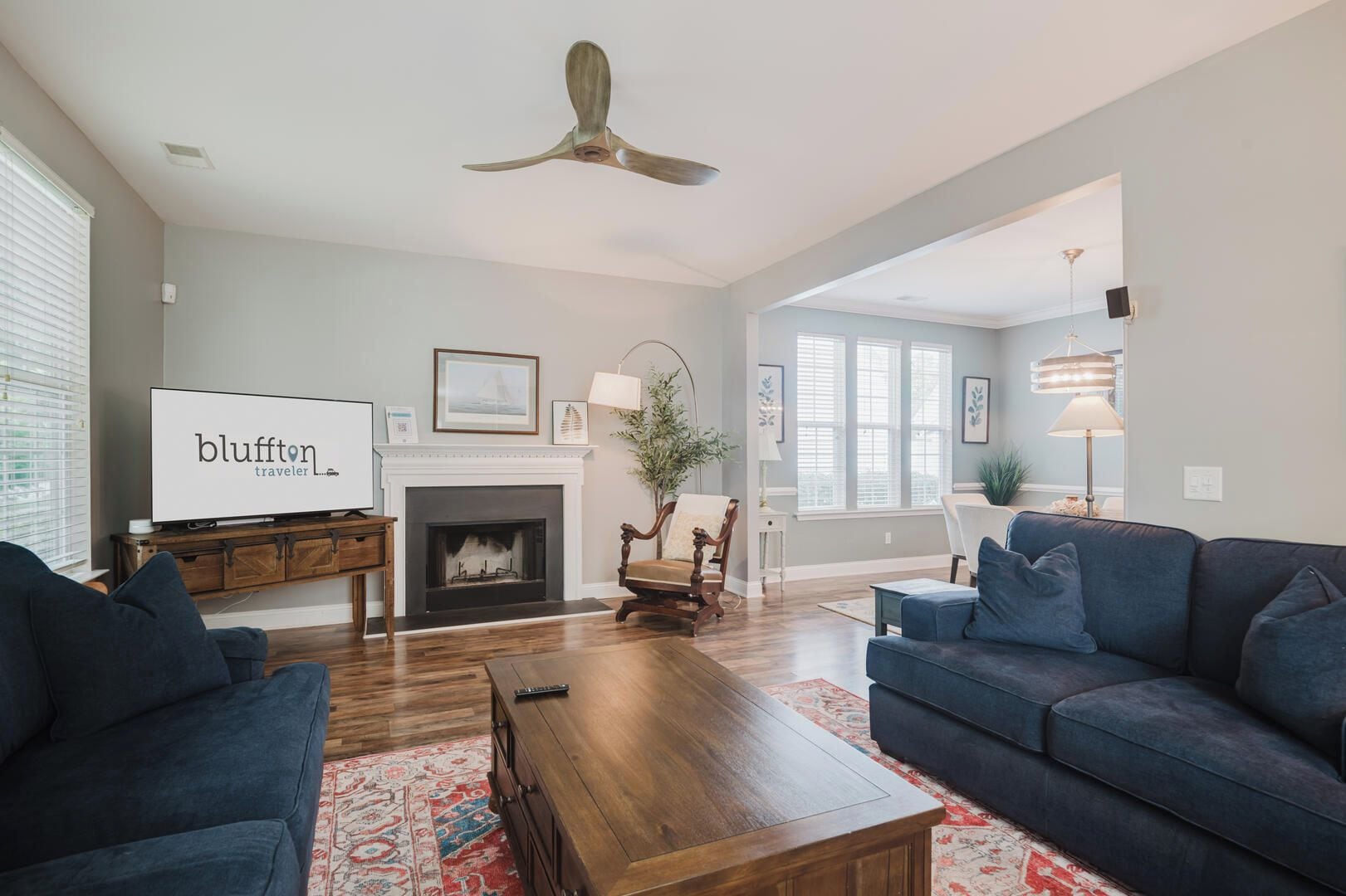 A living room with a fireplace, a television, a ceiling fan, and a large window.