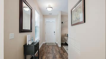 Un couloir avec un plancher en bois, une porte blanche, une console noire sur laquelle sont posés divers objets, et un tableau encadré accroché au mur.