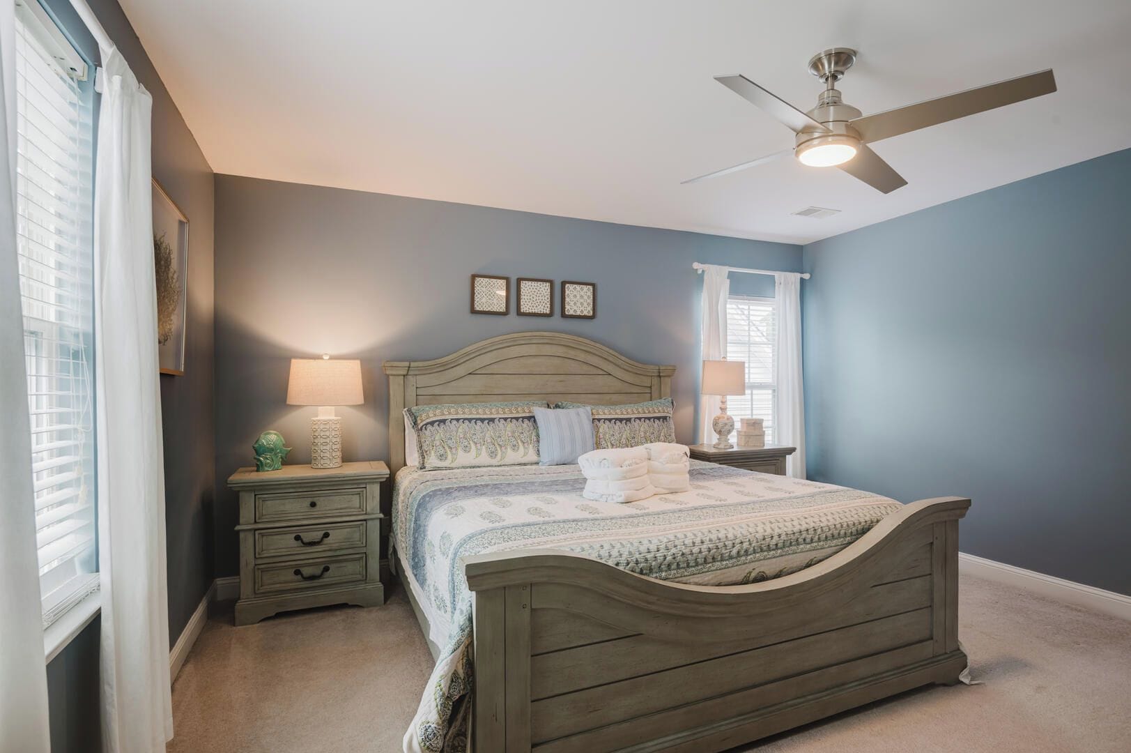 A bedroom with a bed, nightstands, a ceiling fan, and a window with curtains.