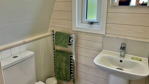 Ett badrum med en toalett, en handduksställning med två handdukar, ett fönster och ett handfat med en spegel ovanför.