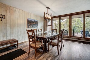 A dining area with a wooden table and chairs, a bench, a painting on the wall, and a large window with a view of trees. - Beautiful 2BR/2BA condo in Keystone, offering a tranquil mountain retreat (Keystone)