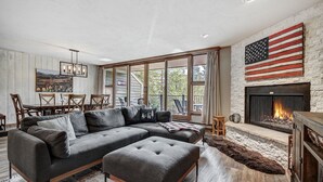 A modern living room with a sectional sofa, a fireplace, and a large window overlooking a deck. - Beautiful 2BR/2BA condo in Keystone, offering a tranquil mountain retreat (Keystone)