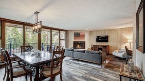 A spacious living area with a fireplace, a large window overlooking greenery, a dining table with chairs, and a cozy seating area. - Beautiful 2BR/2BA condo in Keystone, offering a tranquil mountain retreat (Keystone)