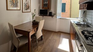 Une cuisine avec des meubles en bois, une cuisinière à gaz, une table à manger avec des chaises et des œuvres d’art encadrées accrochées au mur.