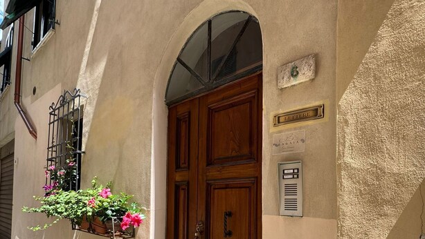 Une entrée d’immeuble avec une porte en bois, une fenêtre dotée d’une grille métallique et une enseigne sur le mur.