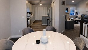 A modern dining area with a marble table, grey upholstered chairs, a white vase, and a chandelier. - Entire Upper Level Home w/Fast Wi-Fi •20 Min SEA, Parking (Kent)