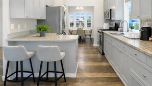 A modern kitchen with white cabinets, a central island with bar stools, and a dining area visible through the window. - Entire Upper Level Home w/Fast Wi-Fi •20 Min SEA, Parking (Kent)