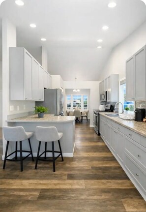 A modern kitchen with white cabinets, a central island with bar stools, and a dining area visible through the window. - Entire Upper Level Home w/Fast Wi-Fi •20 Min SEA, Parking (Kent)