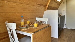 Et lille køkken med trævægge, en hvid stol, et lille spisebord og et morgenmåltid med croissanter og appelsinjuice.