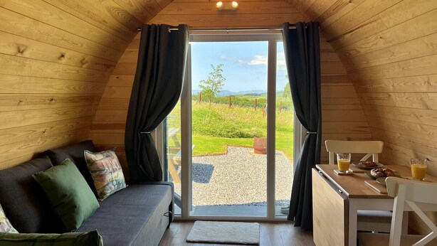 Et hyggeligt rum med trælofter, en skydedør til et udendørs område, en sofa med puder, et lille bord med morgenmad og en stol.
