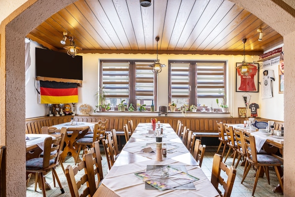 A restaurant with a long wooden table, chairs, and a German flag.