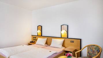 A hotel room with two single beds, bedside tables with lamps, a wooden headboard, a round wooden table, and a floral chair.