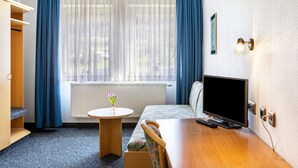 Una habitación de hotel con cama, televisión, una mesita con un florero y un armario.