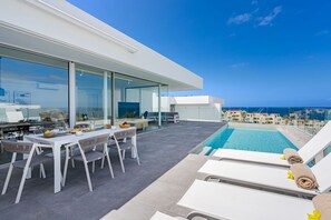 A modern outdoor dining area with a pool, overlooking a coastal cityscape. - Superior Villa 1 - Casangular by Upper (Adeje)