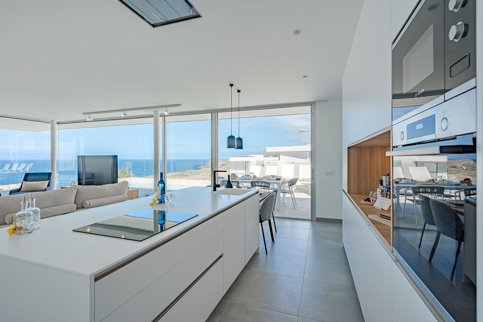 A modern kitchen with a central island, a dining area with a view, and a large window overlooking the sea.