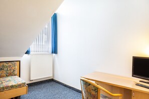 A small, well-lit room with a bed, a desk, a chair, and a television. - Room 'Einzelzimmer' with Wi-Fi (Friedewald)