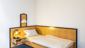 Ein Hotelzimmer mit einem Einzelbett, einem Nachttisch mit Lampe und einem Spiegel.