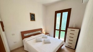 A bedroom with a bed, a nightstand, a dresser, a window, and a wall-mounted picture. - Charming Semi-detached Villa Near the Beach (Valledoria)