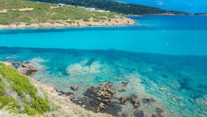 A coastal landscape with clear turquoise waters, rocky shoreline, and a building on the hill. - Charming Semi-detached Villa Near the Beach (Valledoria)