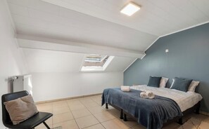 Une chambre avec un plafond en pente, un puits de lumière, un lit avec des oreillers, une chaise et un radiateur.
