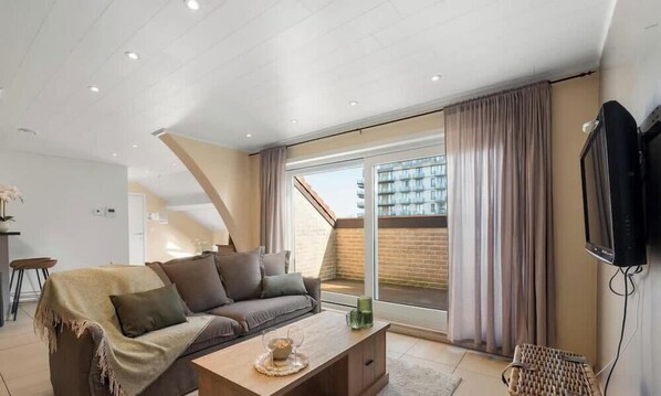 A modern living room with a sofa, coffee table, and a TV. - Esplanade Promenade - stay within walking distance of the beach (De Panne)