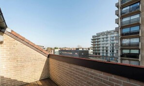 A rooftop terrace with a brick wall and a view of a multi-story building. - Esplanade Promenade - stay within walking distance of the beach (De Panne)